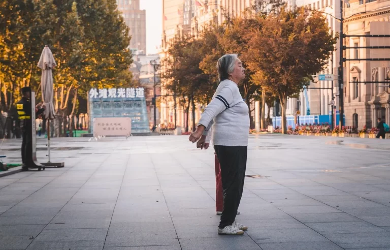 Een oudere vrouw doet rustige oefeningen buiten, passend bij balans, stabiliteit en actief blijven op latere leeftijd.