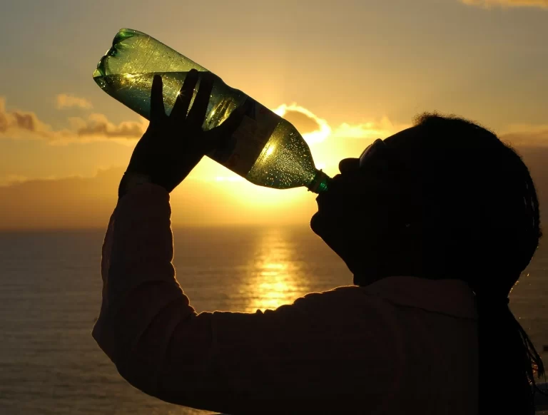 Een oudere drinkt water bij zonsondergang. Regelmatig drinken helpt uitdroging voorkomen, vooral op warme dagen.